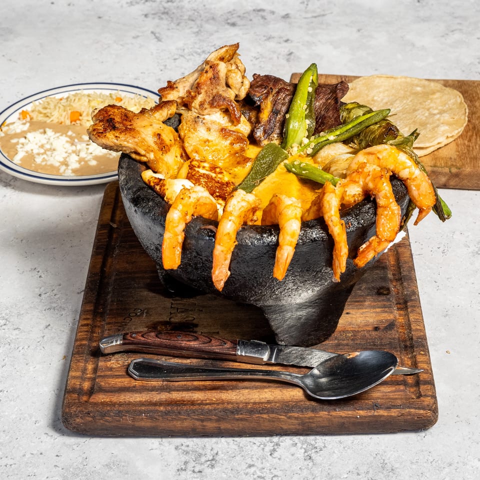 Sizzling platter of grilled shrimp, chicken, steak, cheese, and vegetables served with tortillas, rice, and beans.