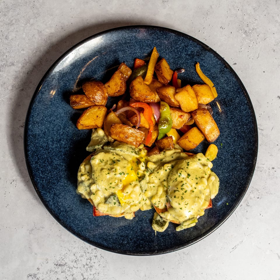 Blue plate of roasted potatoes and colorful peppers alongside creamy herb-topped chicken or vegetables.
