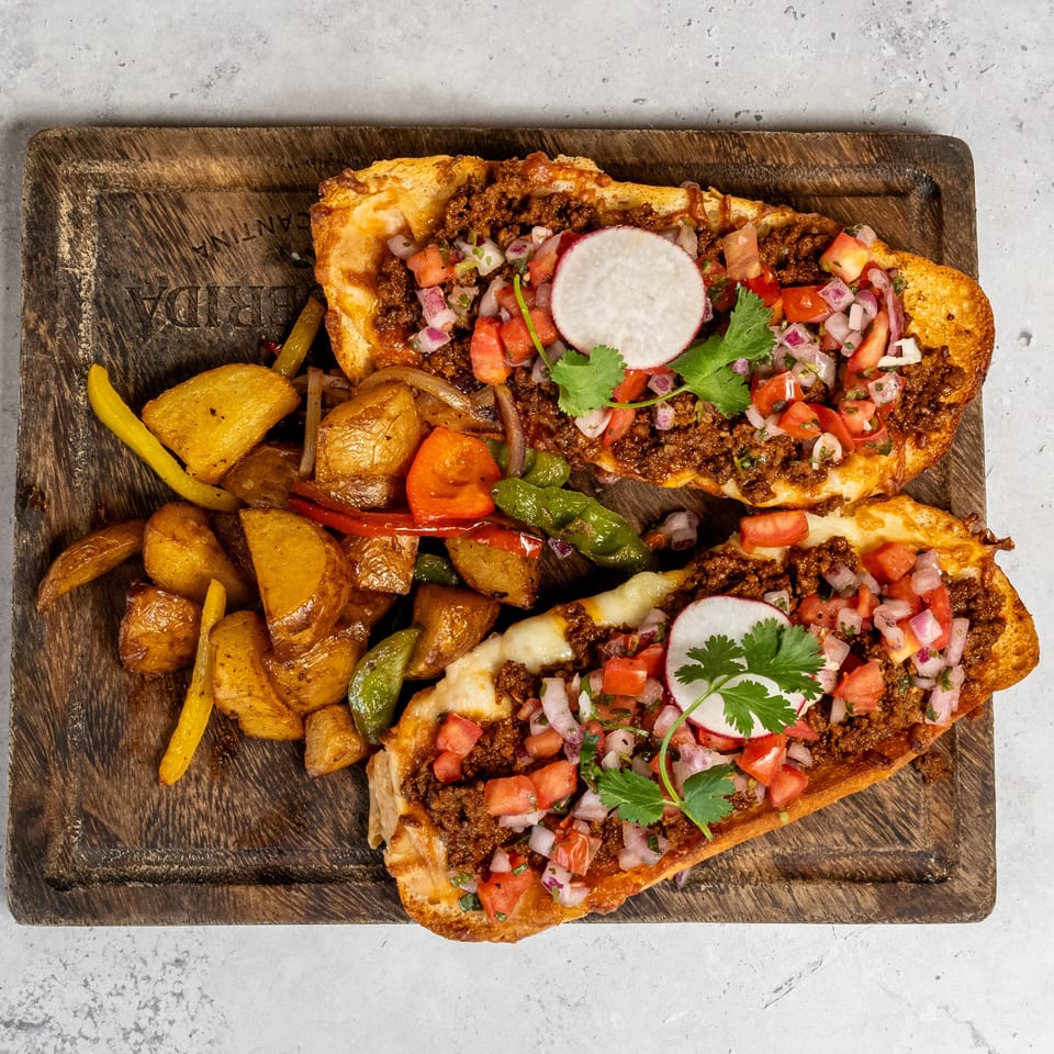 Two loaded flatbreads topped with seasoned beef, cheese, pico de gallo, radishes, and cilantro, served with roasted potatoes and peppers.