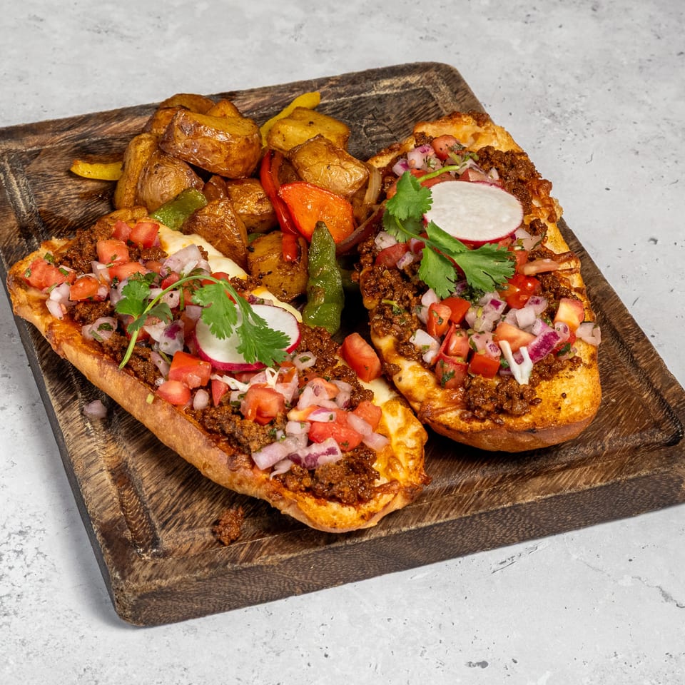 Two open-faced sandwiches topped with spiced ground meat, pico de gallo, radishes, and cilantro, served with roasted potatoes and peppers.