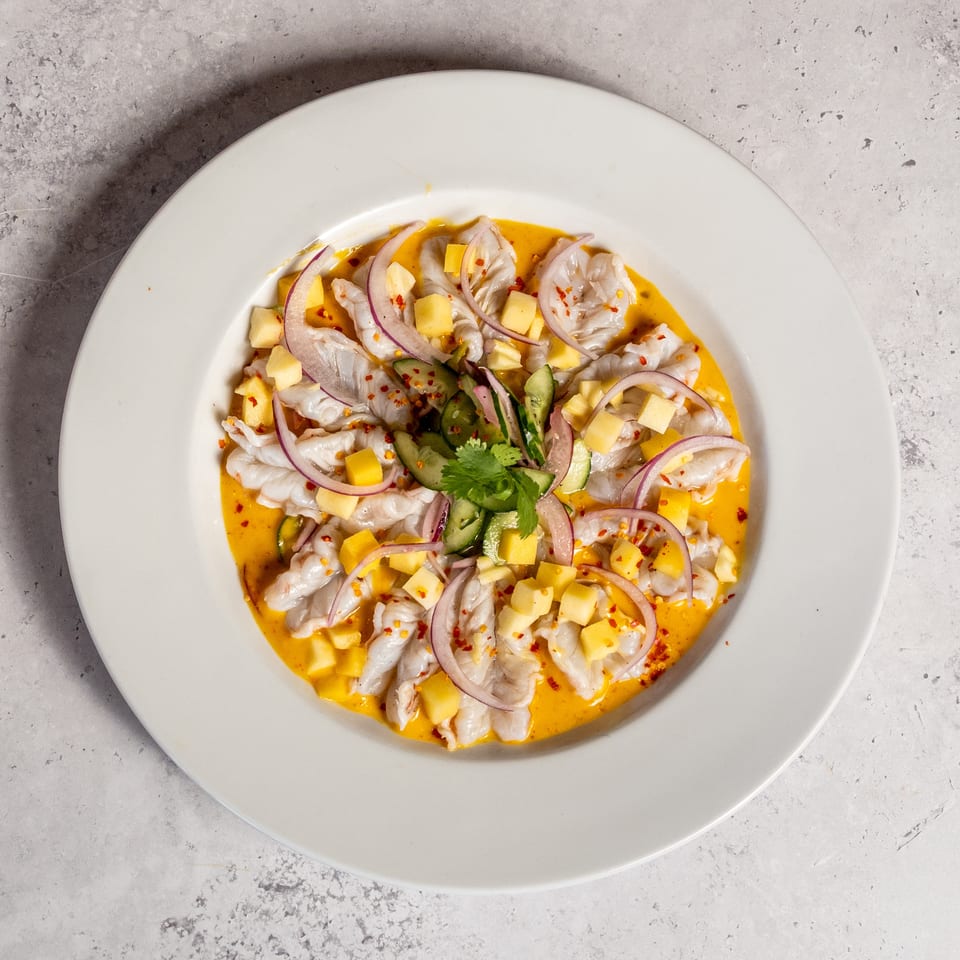 Overhead view of shrimp ceviche with mango, cucumber, red onion, cilantro, and chili flakes in orange sauce.